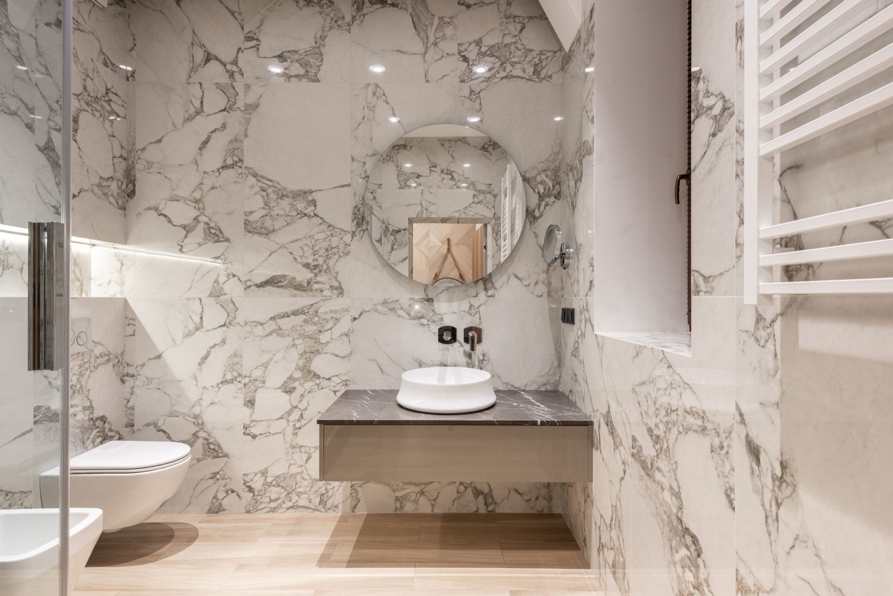 A bathroom wall clad in book-matched marble-effect slab porcelain behind a countertop basin