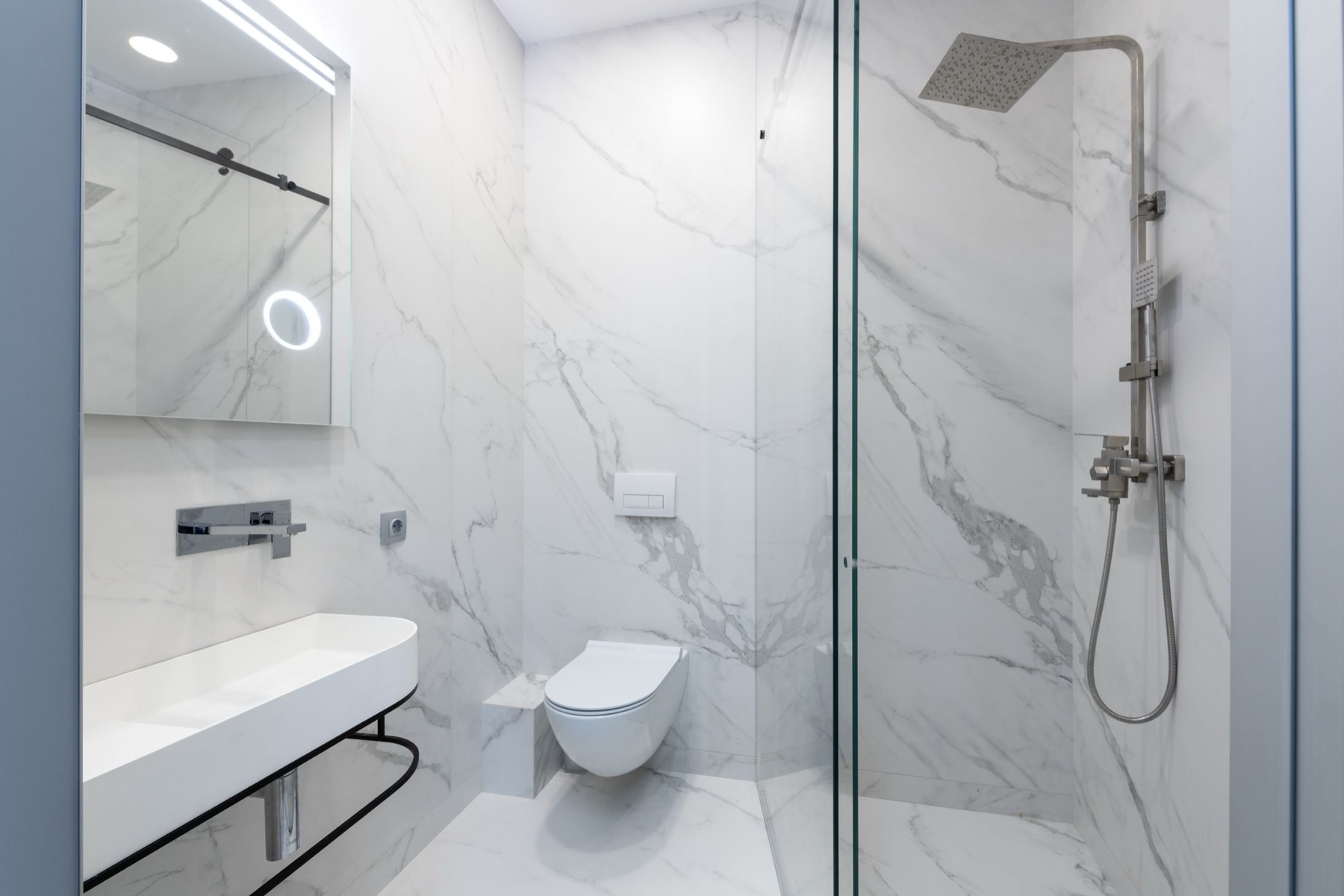 A compact shower room tiled floor-to-ceiling in marble-effect porcelain with a glass screen