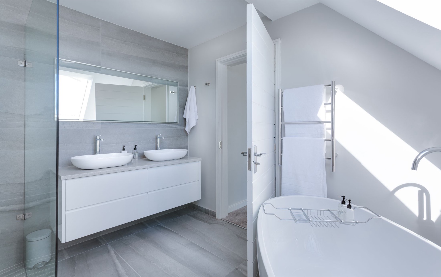 A bright bathroom with twin basins and a grey wood-effect plank tiled floor